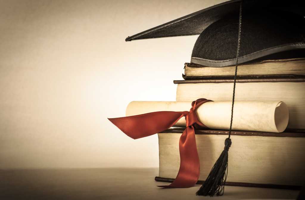 graduation cap with diploma stacked on books