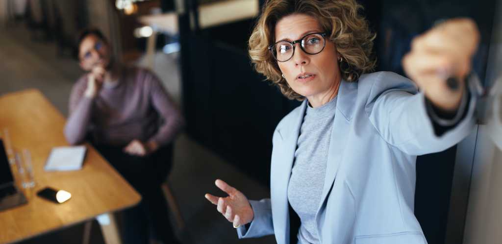 Business woman pitching an idea to her team in a meeting. Mature business woman giving a presentation in a boardroom. Team of professionals working together in a modern workplace.